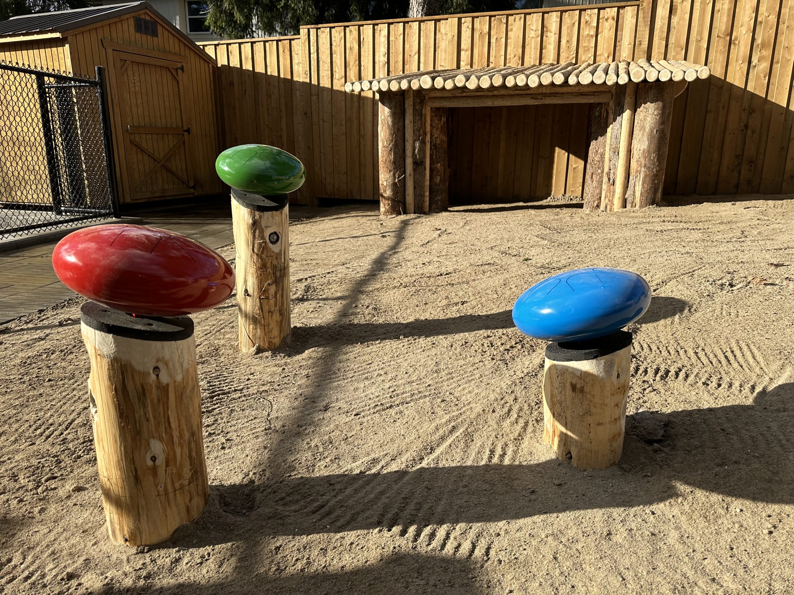 Colorful outdoor musical tongue drums mounted on wooden posts in a sand play area