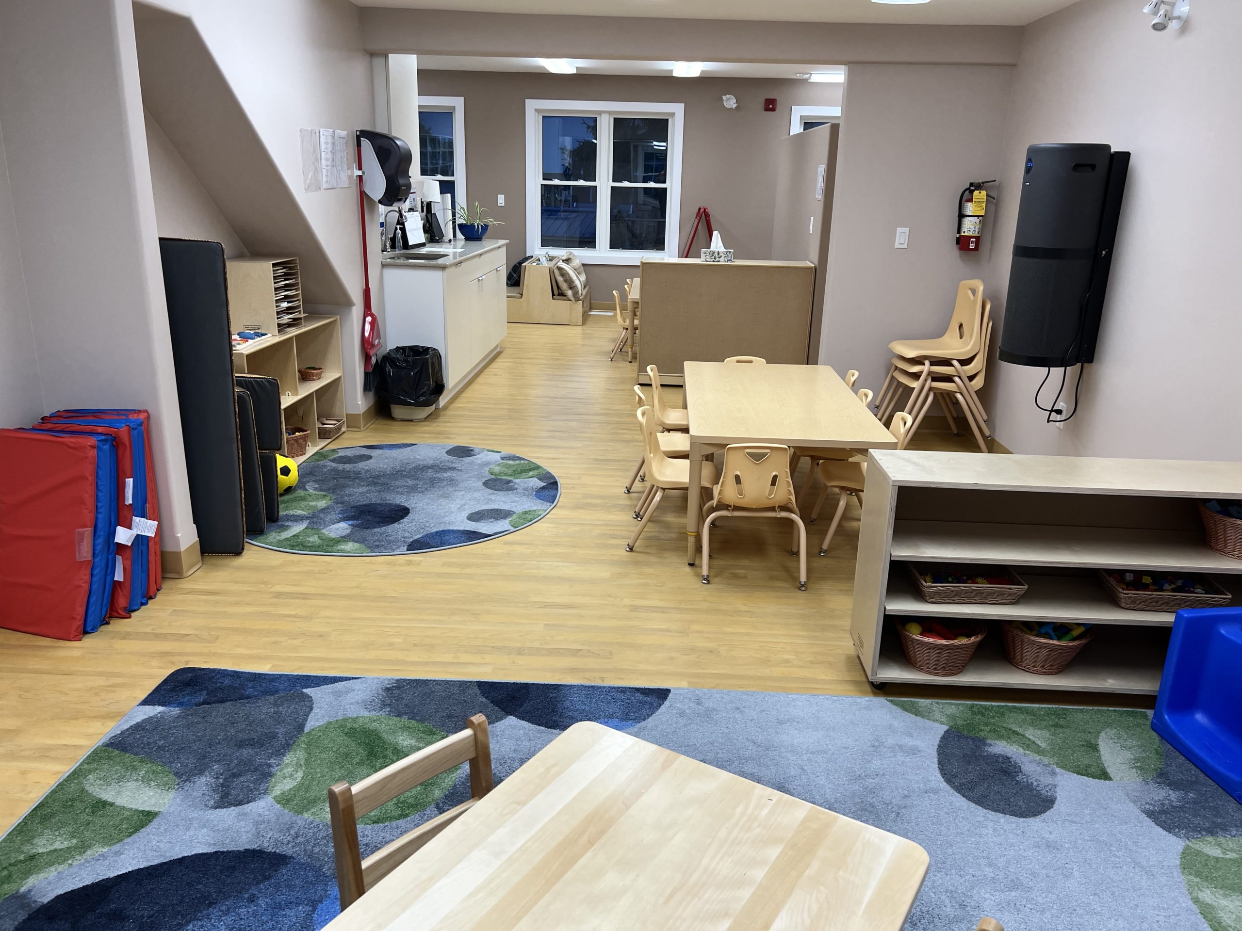Classroom corner with wooden play kitchen, tables, red easel, and shelving