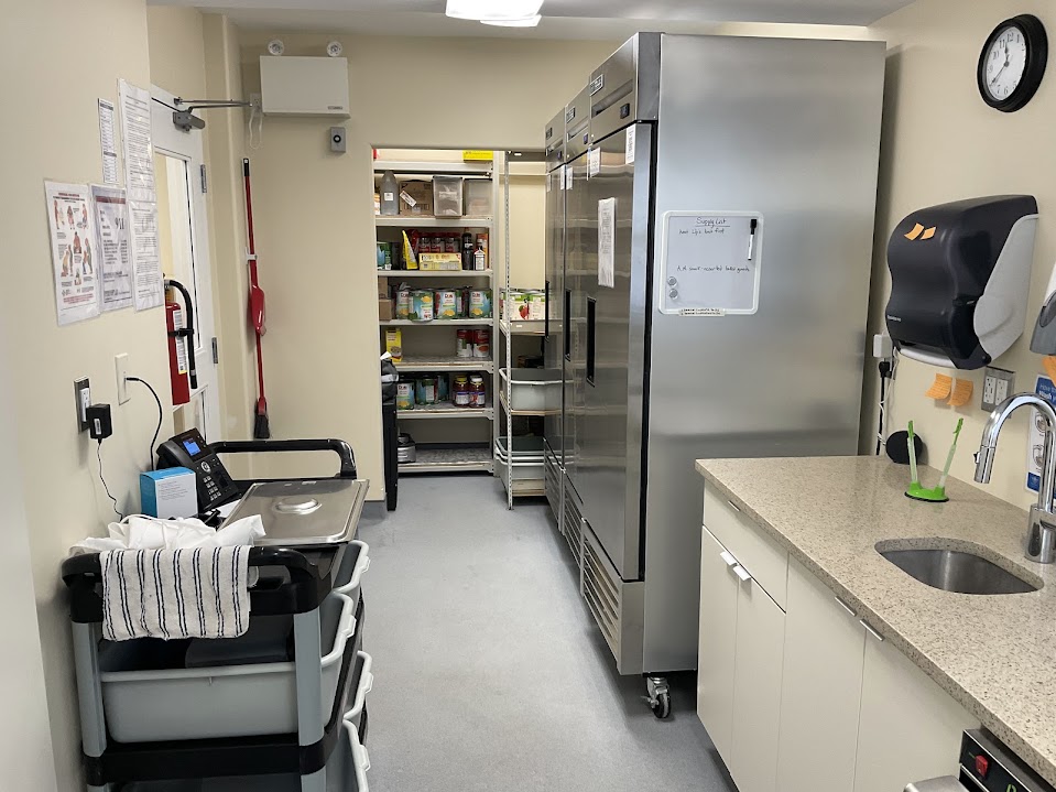 Kitchen storage room with stainless fridge, stocked pantry shelving, and sink counter
