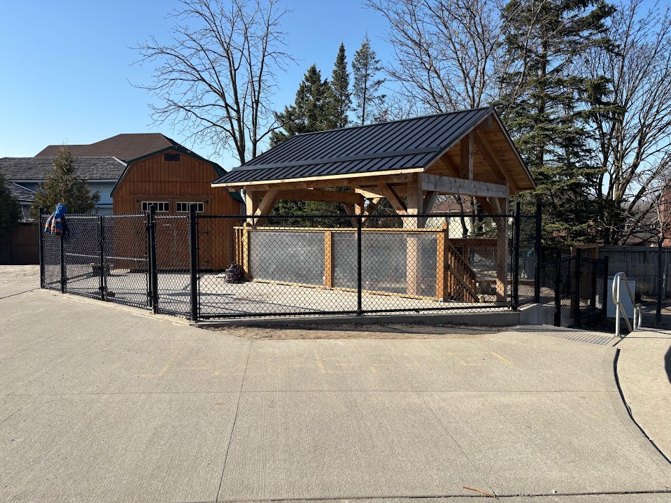 Wide exterior view of the fenced outdoor play yard and pavilion beside the school building
