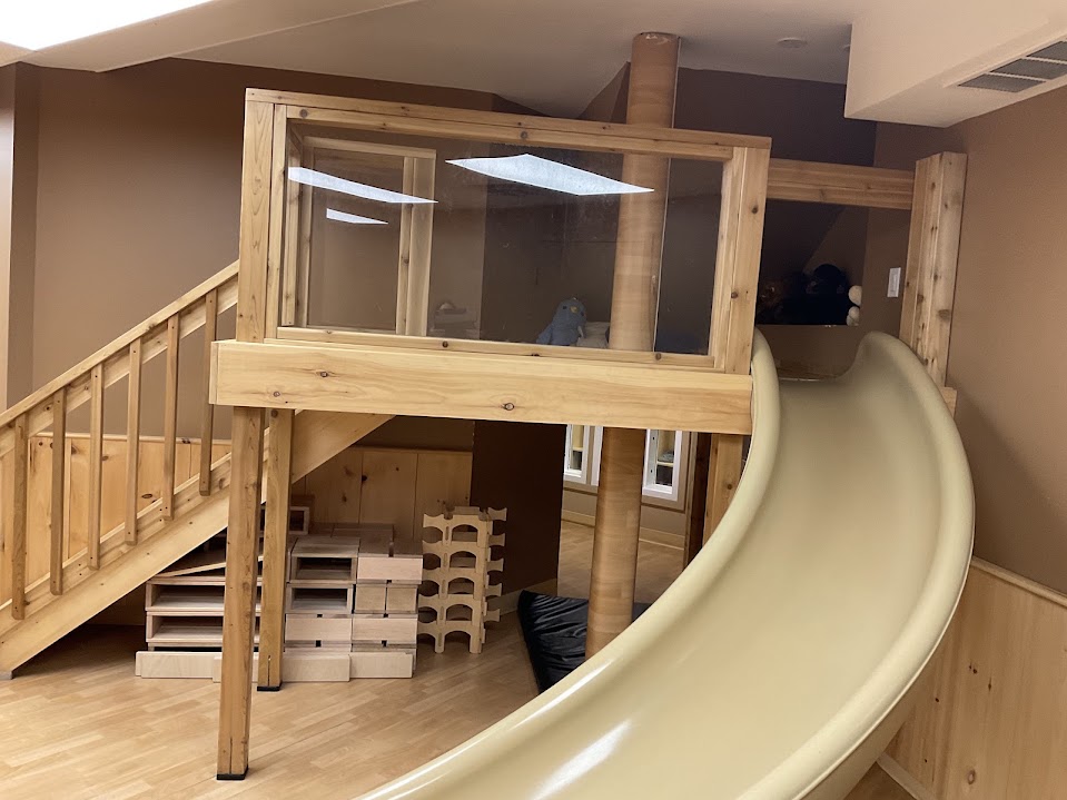 Wooden loft structure with stairs leading up to a glass-walled lookout and a curved slide coming down