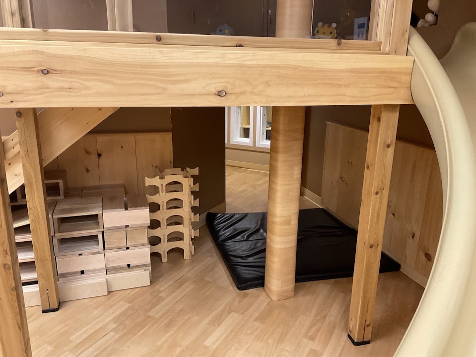 View beneath the loft near the slide with wooden storage crates and a black cushioned mat
