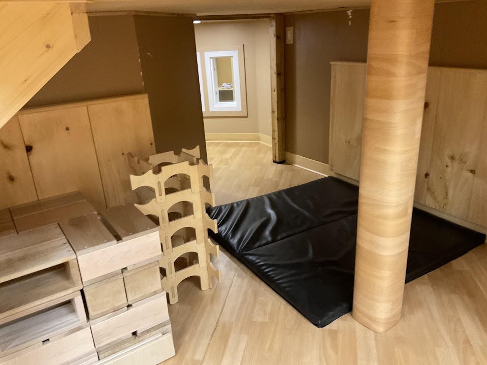 Storage area beneath the loft with wooden block storage, a toy rack, and cushioned mats on the floor