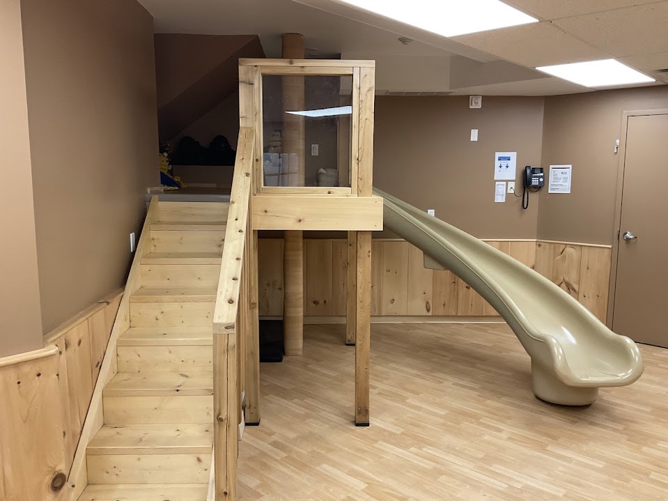 Wooden loft structure with stairs leading up to a glass-walled lookout and a curved slide coming down