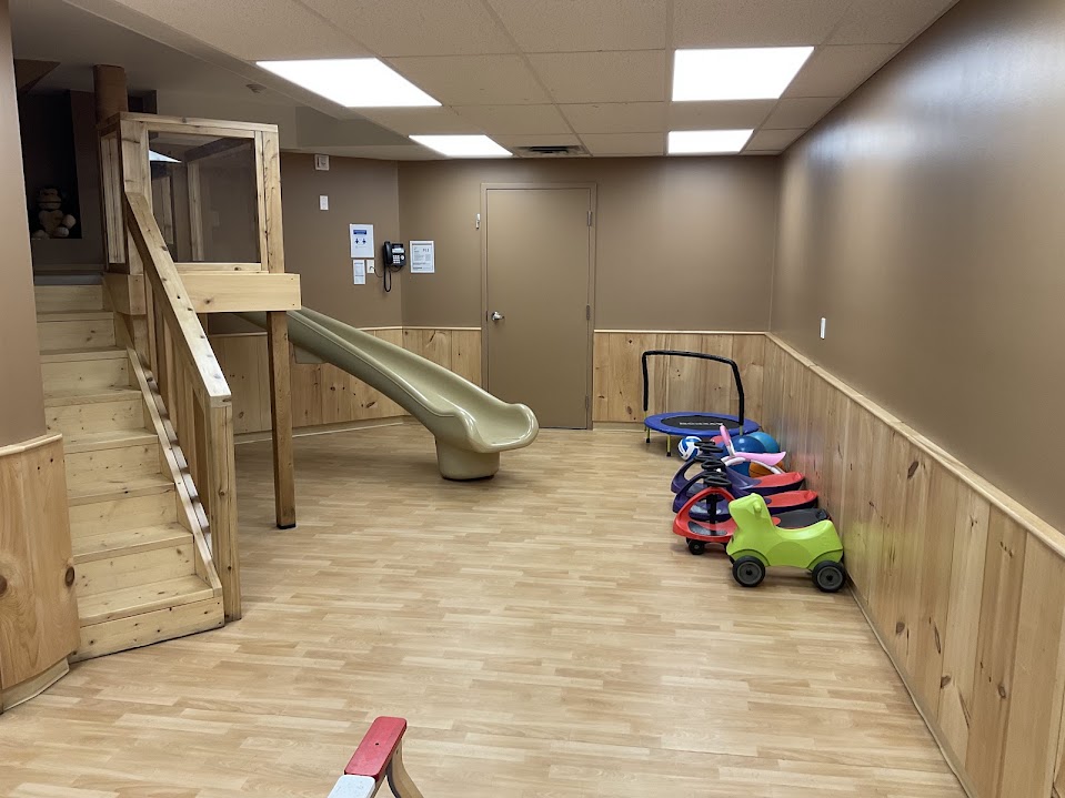 Gross motor room with the loft and slide, ride-on toys, and a mini trampoline along the wall