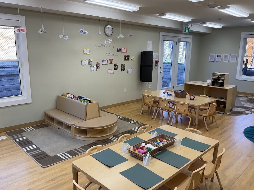 Classroom with activity tables, play kitchen corner, and round rug