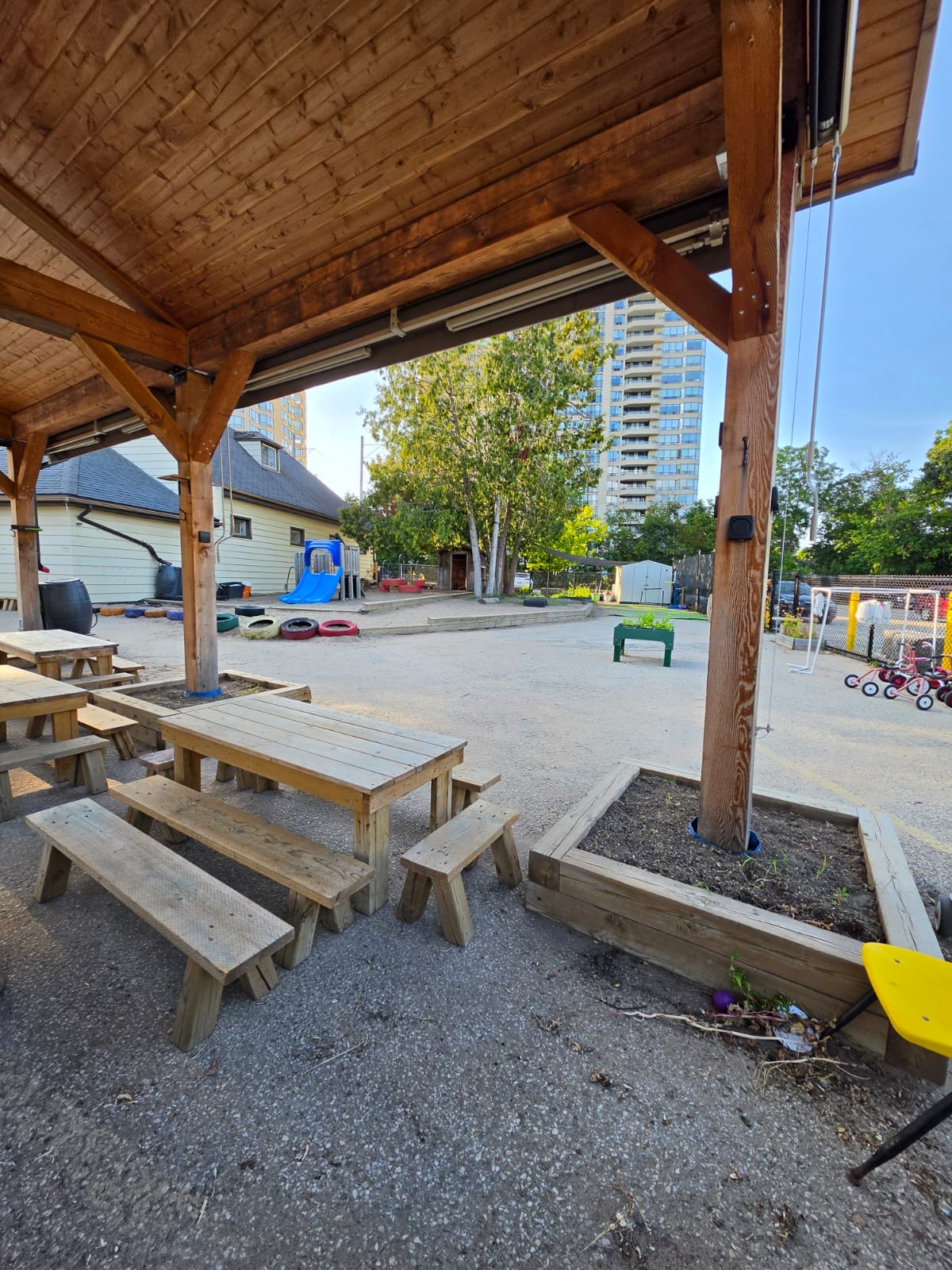 Pavilion with picnic tables beside a play area with a slide, tires, and tricycles