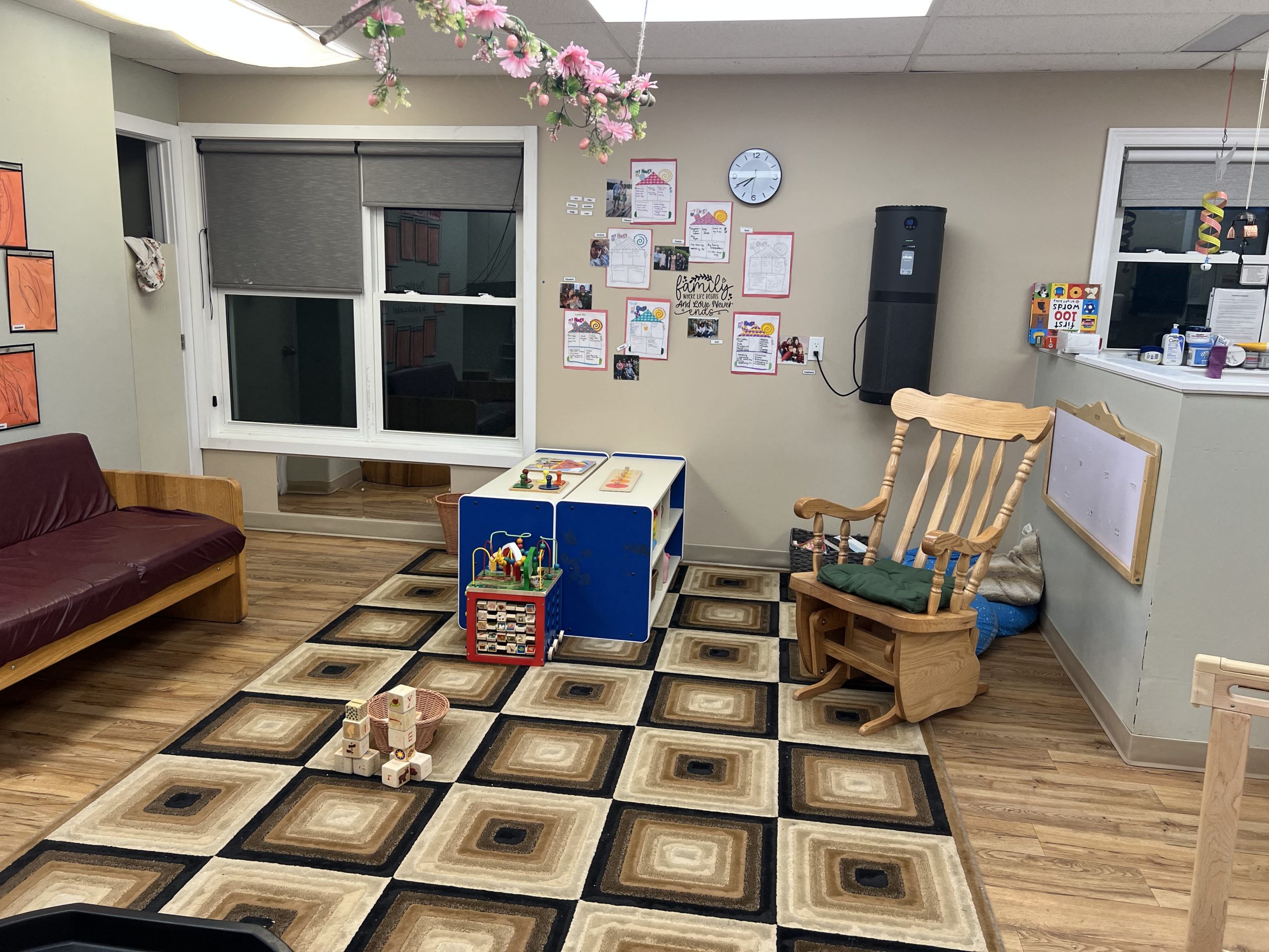 Open infant playroom with a couch, children's artwork on the wall and a sensory tray