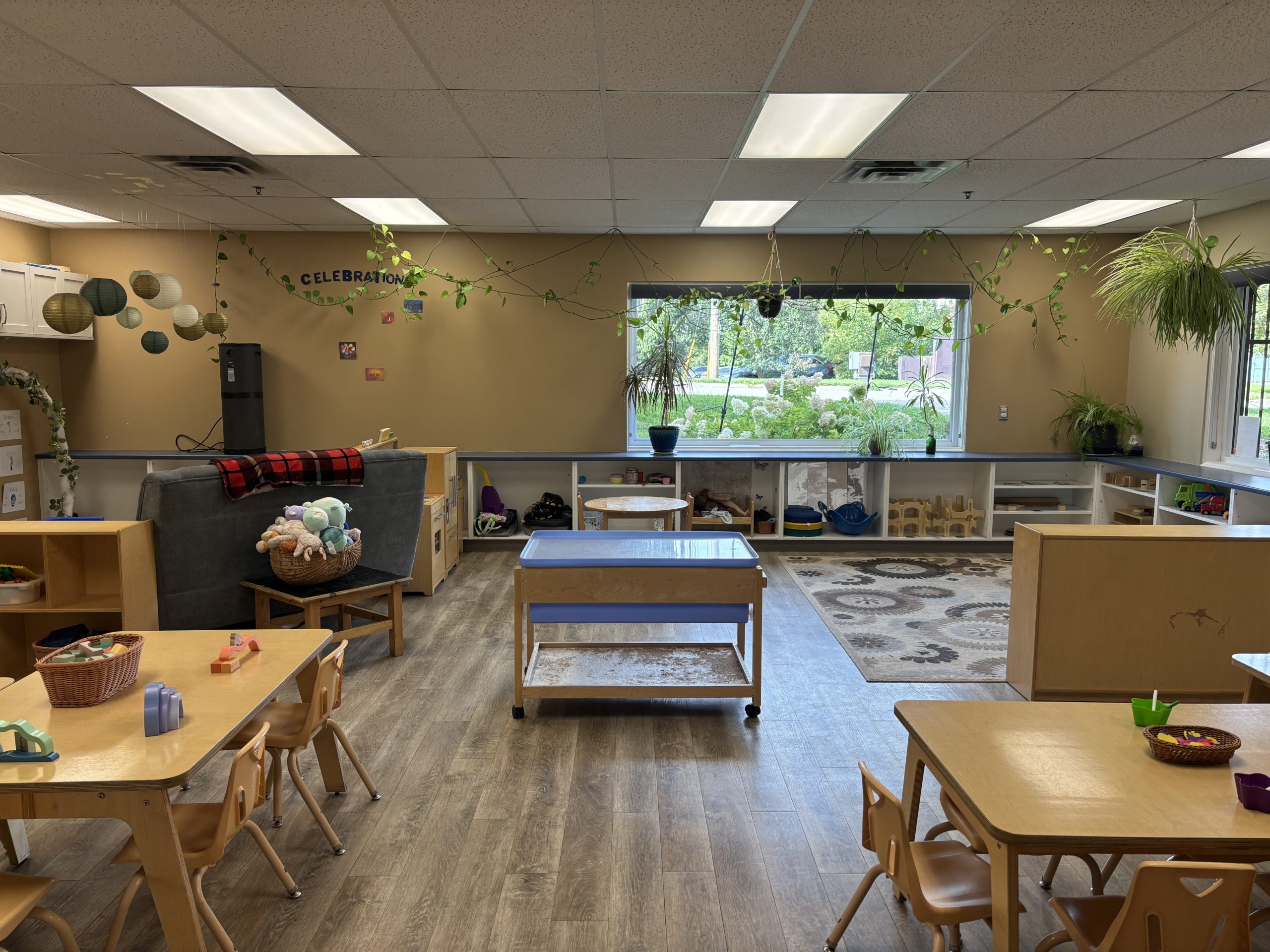 Classroom with a sensory table in the centre, trailing plants and a large window looking onto greenery