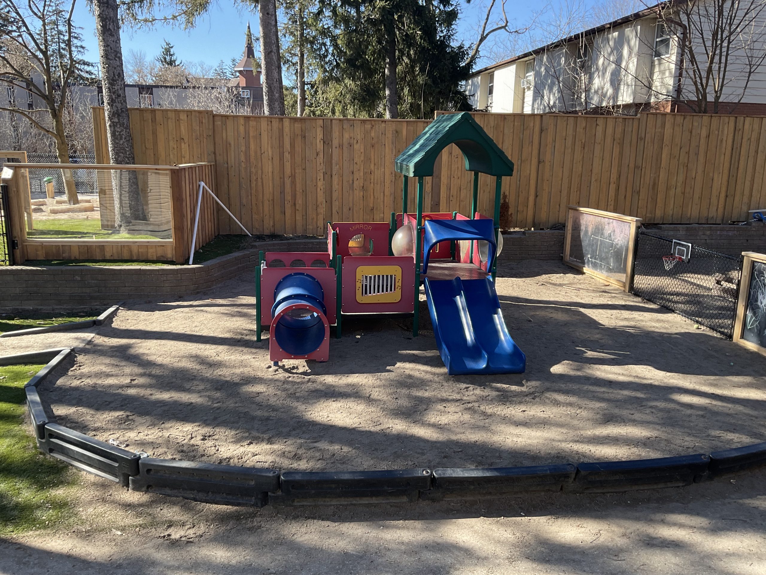 Compact play structure with tunnels, a mirror panel, and a double slide in a sand pit