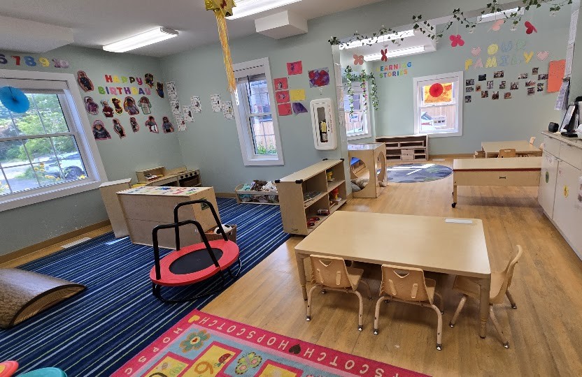 Bright playroom with large windows, a colourful hopscotch number rug, a child-sized table and chairs, and children's artwork on the walls