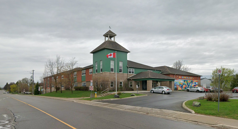 KW Bilingual School building, a green and red-brick two-storey school with a white cupola, a Canadian flag out front and a colourful mural by the entrance